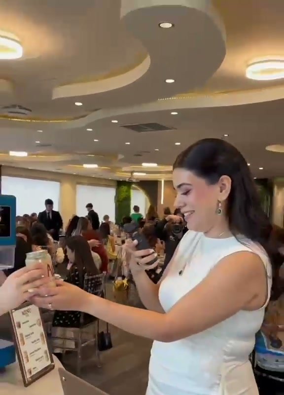 Invitada recibiendo una lata de ACAM en un salón lleno de gente.